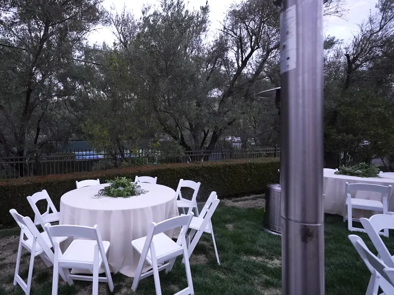 White linen round tables and folding chairs set on a shaded lawn for a San Leandro gathering