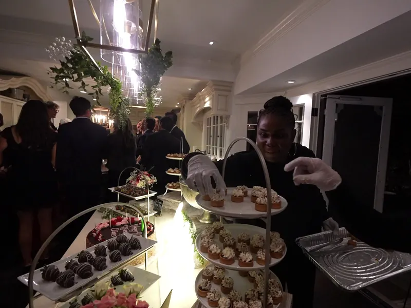 Server presenting tiered desserts along a greenery-lined hallway at a Rodeo celebration