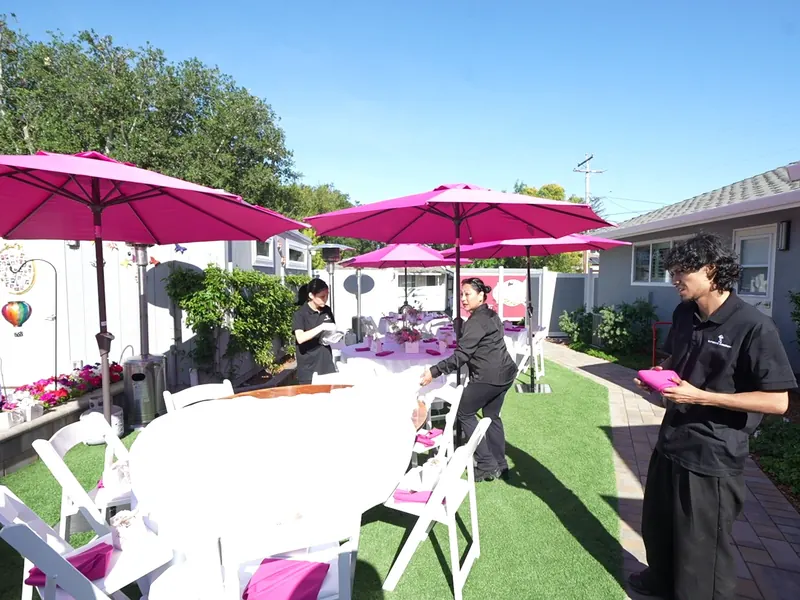 Catering staff setting a lawn buffet table under pink umbrellas at an Oakland backyard event