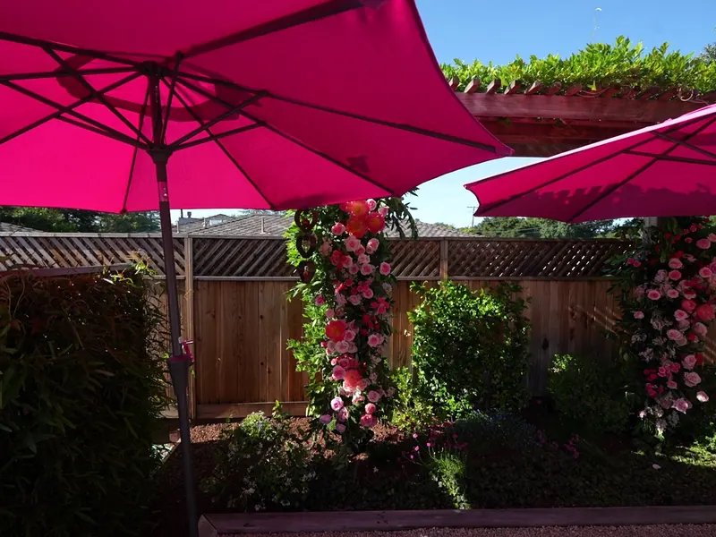 Rose-covered floral arch framed by pink umbrellas at an Alameda garden celebration