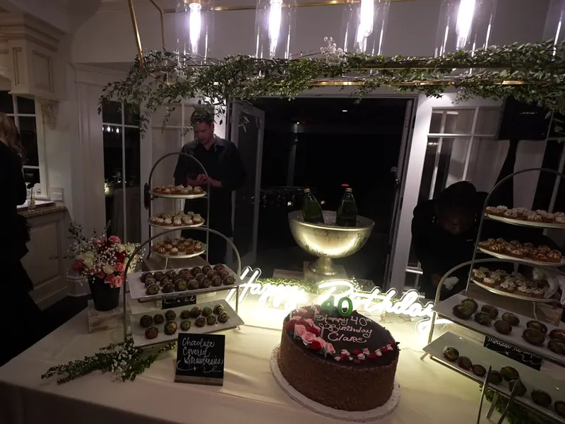 Greenery-draped birthday dessert display with a neon sign and layered cake at a Richmond party