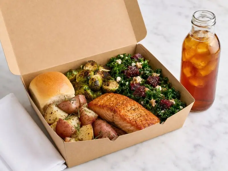 Oakland Catering Company grab-and-go lunch box filled with salmon, roasted produce, kale and beet salad, and a soft roll.