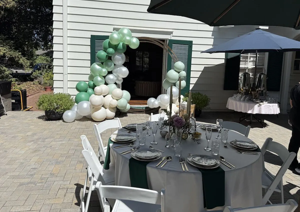 Sage and ivory balloon garland arcing across a doorway beside a fully styled table — balloon and bloom styling for Oakland and Richmond celebrations